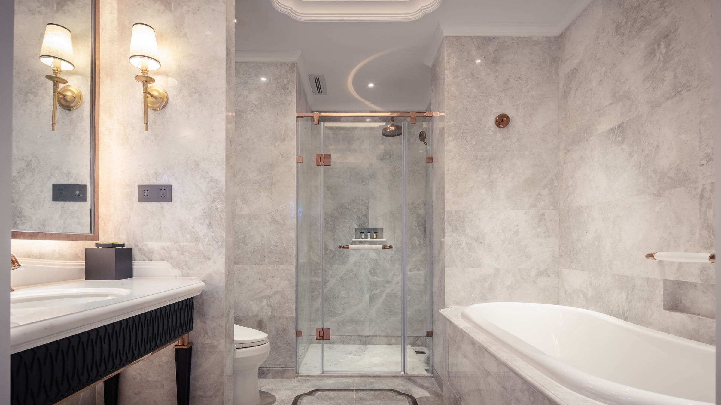 A finished bathroom in stone tile with a glass shower, tub and brass fittings